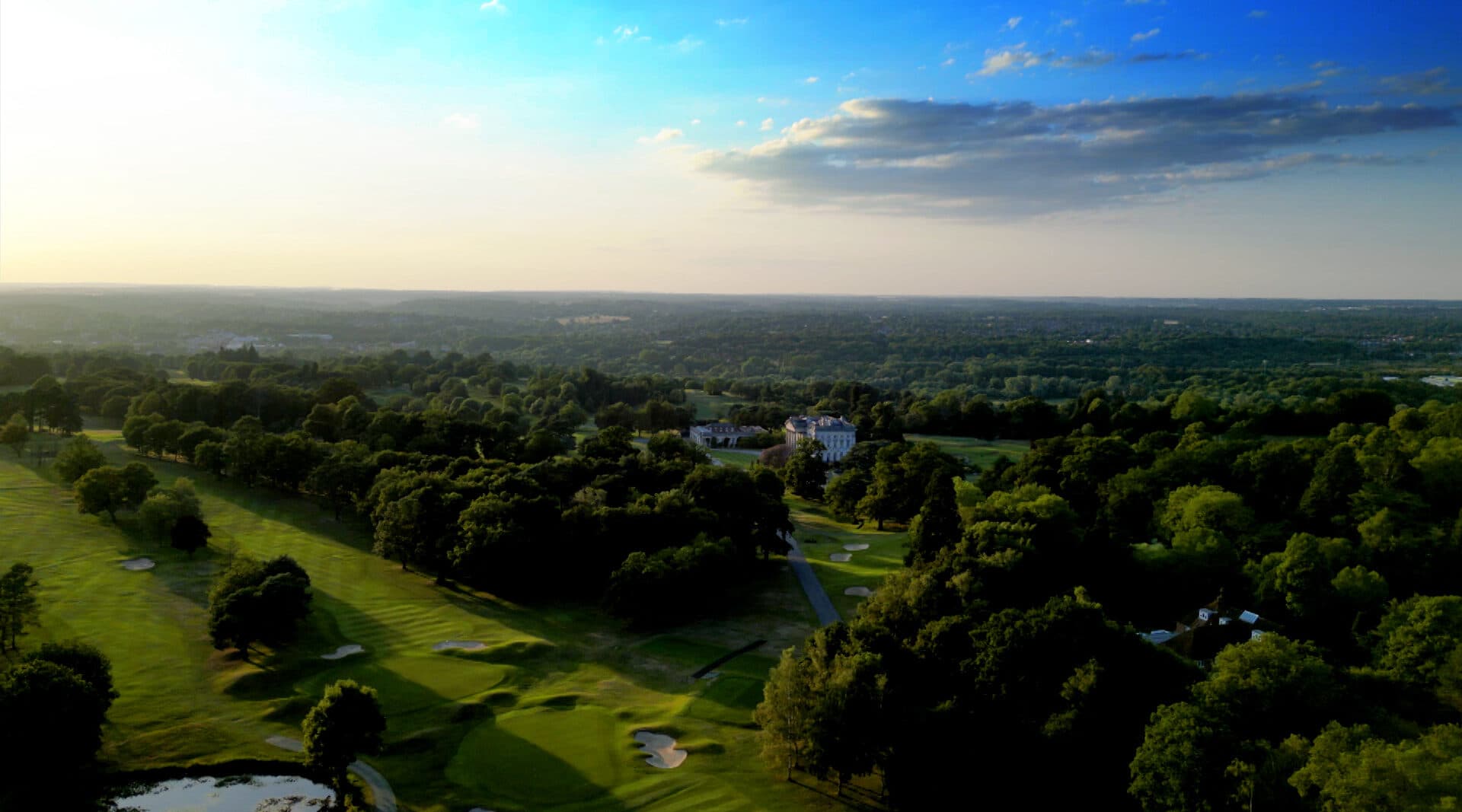 Aerial view across Moor Park's golf course towards the mansion clubhouse in warm light
